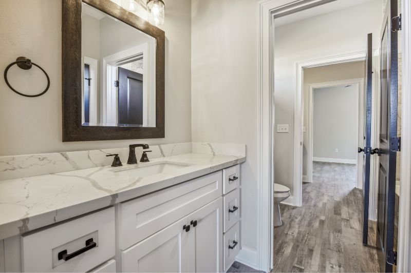 Bathroom with white vanity, marble countertop, black fixtures, and a hallway visible in the background.