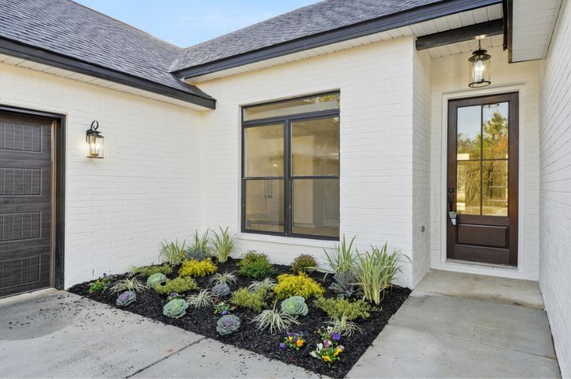 White brick house with a dark door, black-framed window, and a small garden.