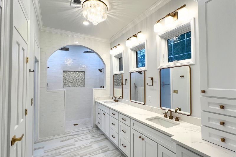 Bright white luxury bathroom with double sinks, mirrors, and arched shower.