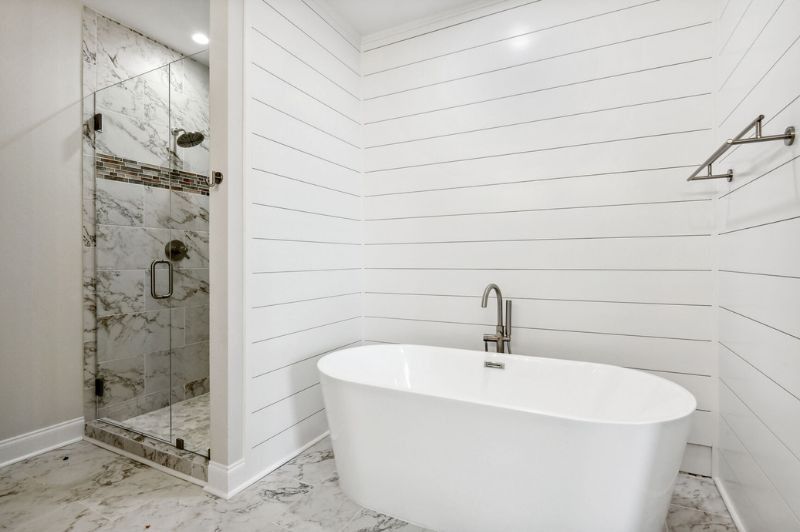 Bathroom with white shiplap walls, a freestanding tub, and a marble shower.
