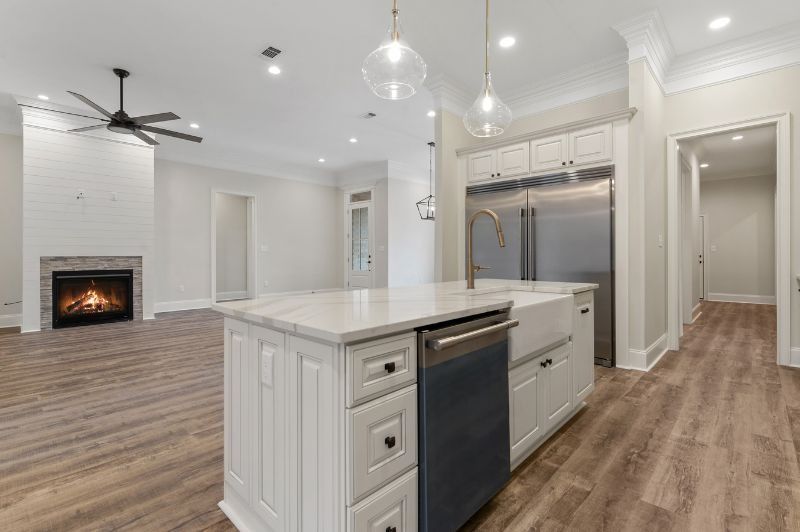 Open-concept kitchen with a white island, stainless steel appliances, fireplace, and wooden floors.