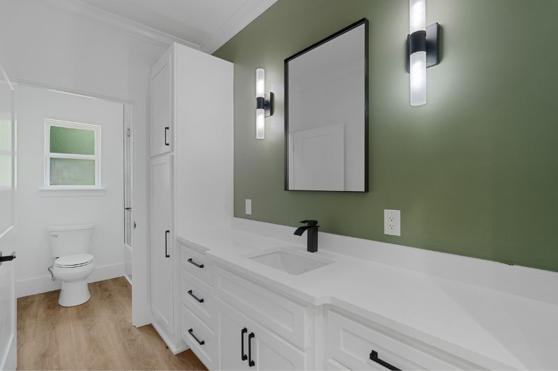 Modern bathroom with white vanity, black fixtures, and green accent wall.