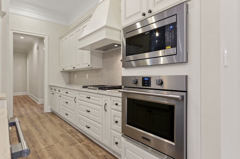 White kitchen with stainless steel microwave/oven, cabinetry, and wooden floor.