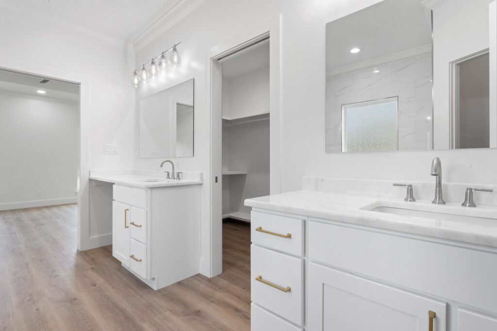 White bathroom with double vanity, closet, and hardwood floors.