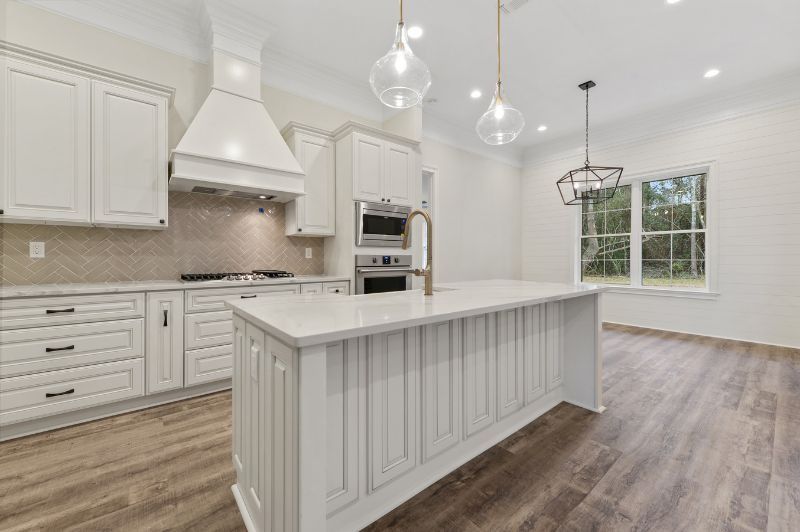 White kitchen with island, cabinets, and range; glass pendant lights; window.