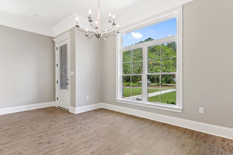 Empty room with large window, chandelier, and neutral walls and flooring.