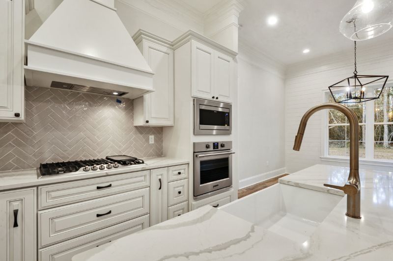 White kitchen with marble countertops, stainless steel appliances, and gold faucet.