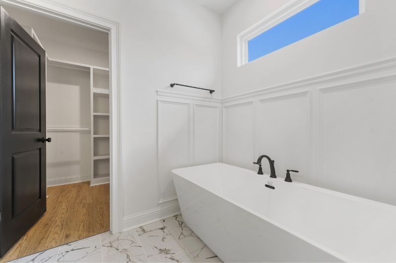 Bright white bathroom with a modern tub and walk-in closet. Black door and fixtures.