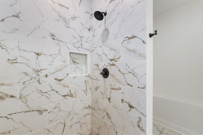 Shower with marble-look tile, black fixtures, and a built-in shelf.