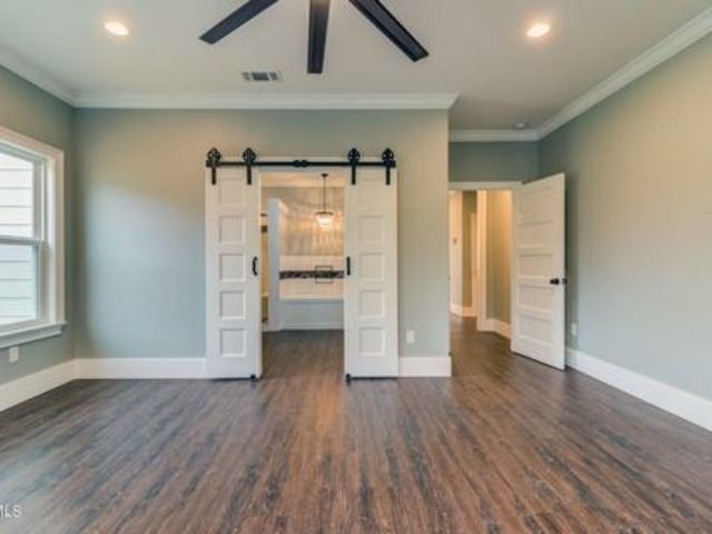 Spacious room with dark wood floors, light green walls, white trim, and barn doors leading to another room.