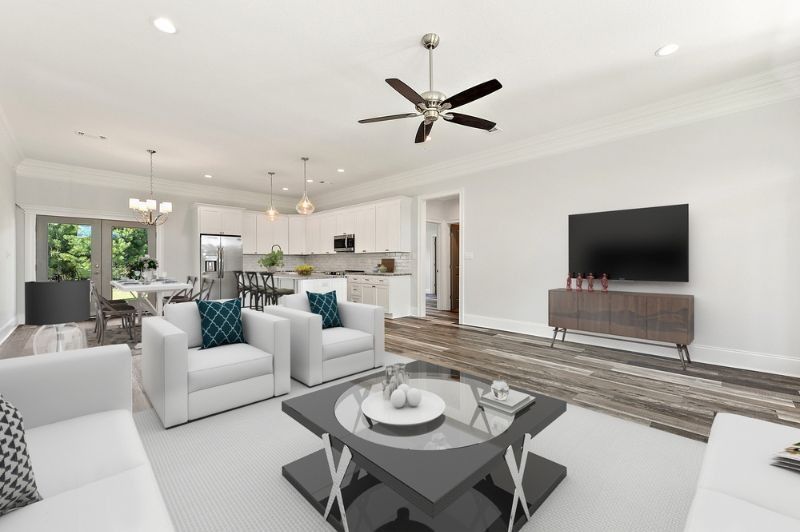 Spacious living room with white furniture, open to kitchen and dining area; features TV, coffee table, and ceiling fan.