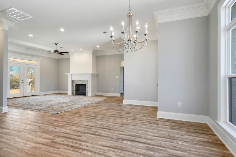 Spacious, light-filled living room with fireplace, chandelier, and hardwood floors. Light gray walls, white trim.