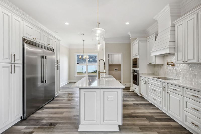 White kitchen with stainless steel appliances, island, and light-colored wood floors.