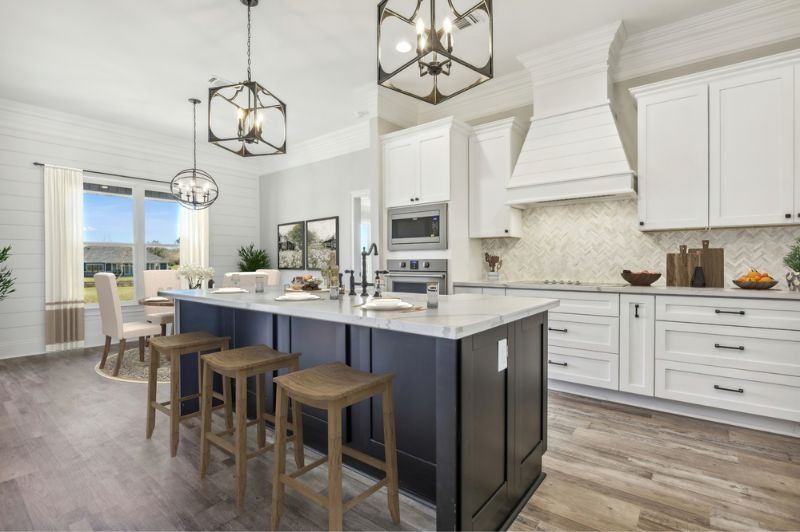 Modern kitchen with white cabinets, navy island, and wood flooring.
