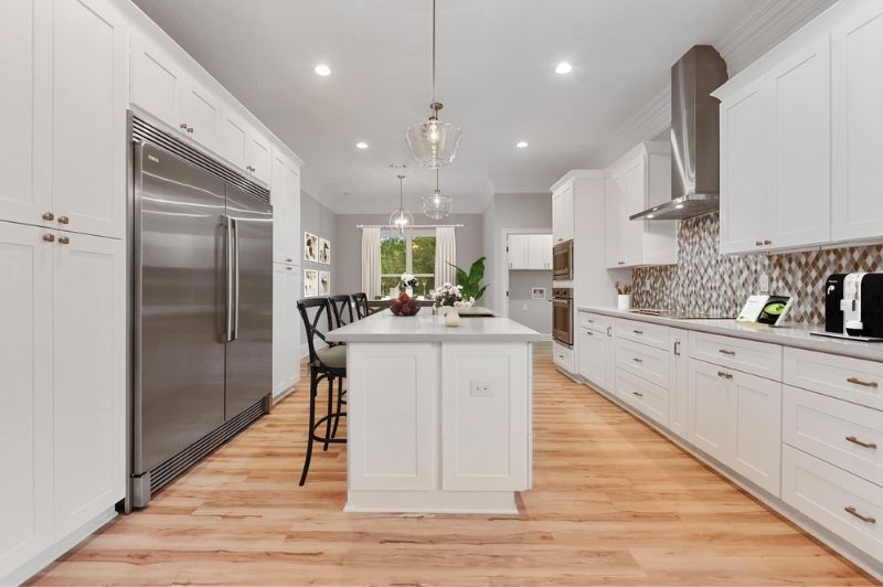 Bright white kitchen with stainless steel appliances, island, and light wood floors.