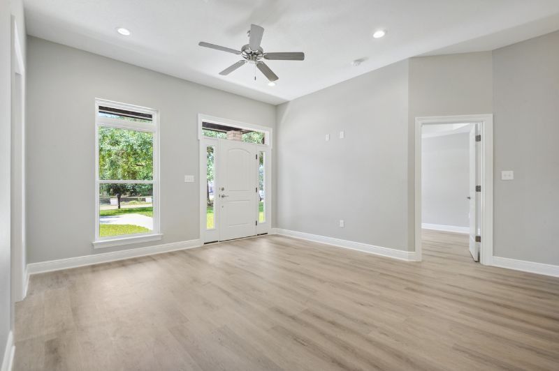 Empty room with light gray walls, wood-look flooring, white door and windows.