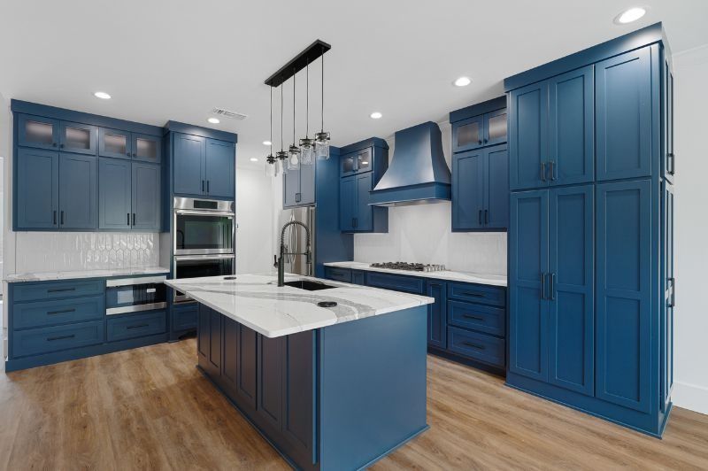 Blue kitchen with white countertops and wood floors; island in the center.