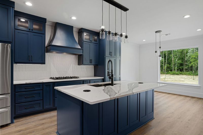 Navy blue kitchen with island, white countertops, and large window overlooking trees.