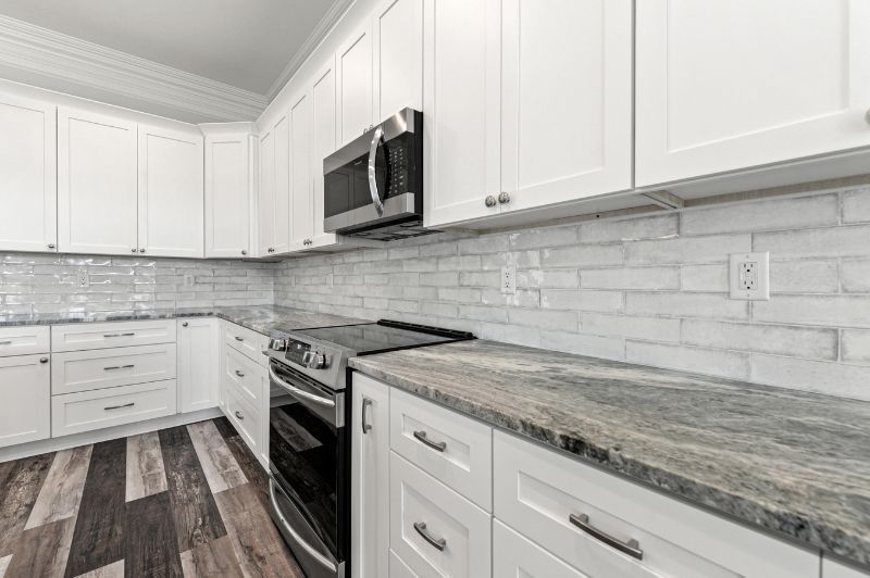 White kitchen with stainless steel appliances, grey countertops, and patterned wood floor.