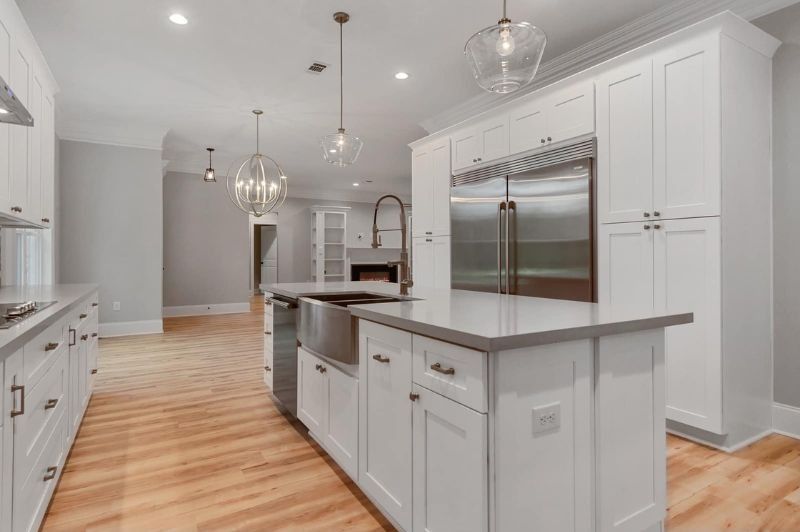 White kitchen with island, stainless steel appliances, light gray walls, and wooden floors.