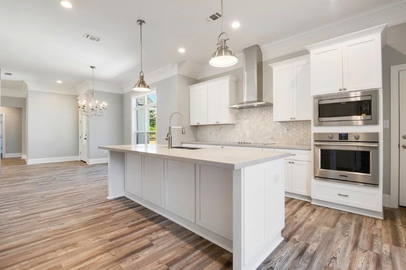 Modern white kitchen with island, stainless steel appliances, and light wood floors.