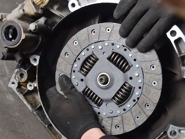 A person wearing black gloves is holding a clutch plate