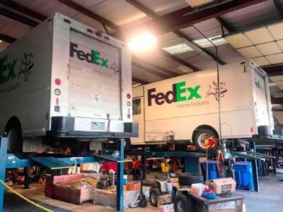 Two fedex trucks are sitting on a lift in a garage.