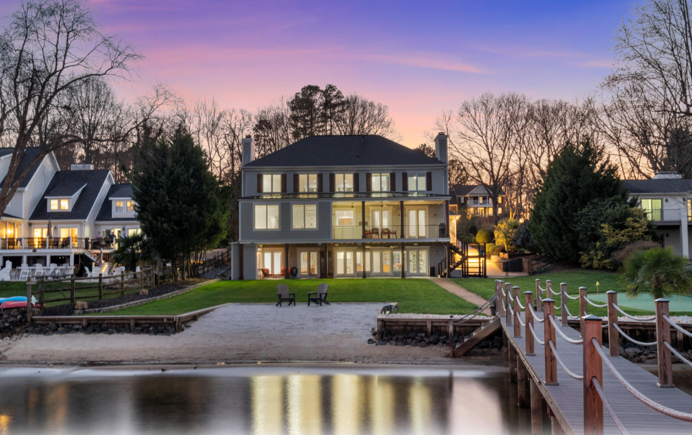 Two-story luxury home with illuminated windows, set against a dramatic purple and pink sunset sky.