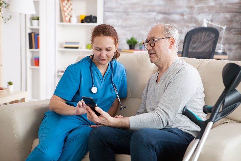 A nurse is helping an elderly man with crutches use a cell phone.