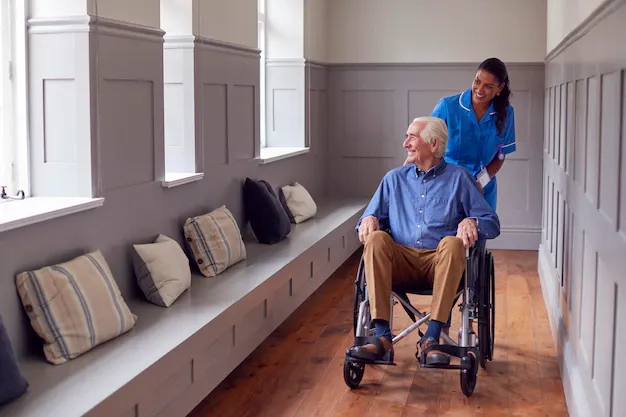 A senior man being pushed by a caregiver in a wheelchair.