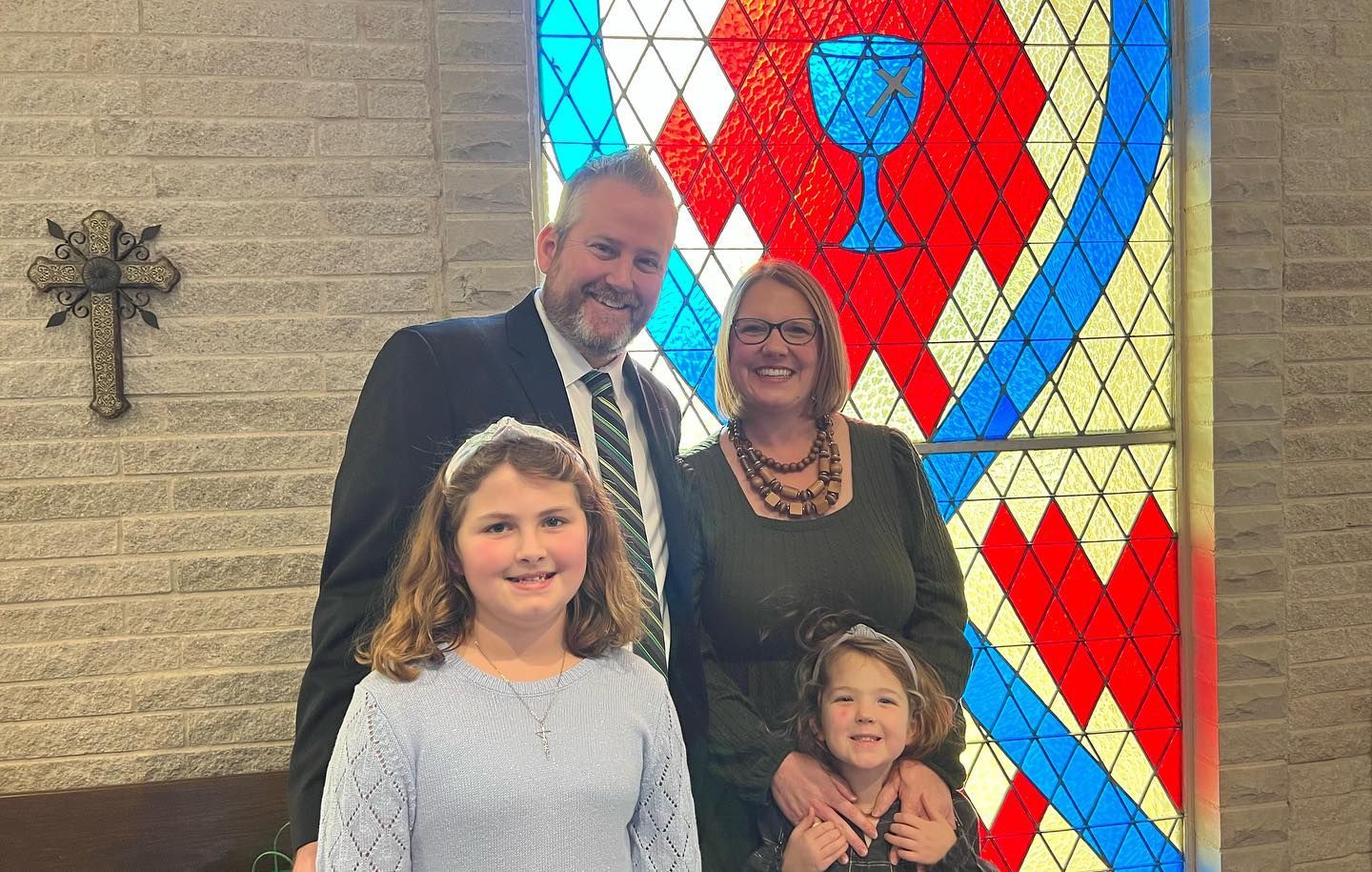 Family posing in front of stained-glass window with a chalice.