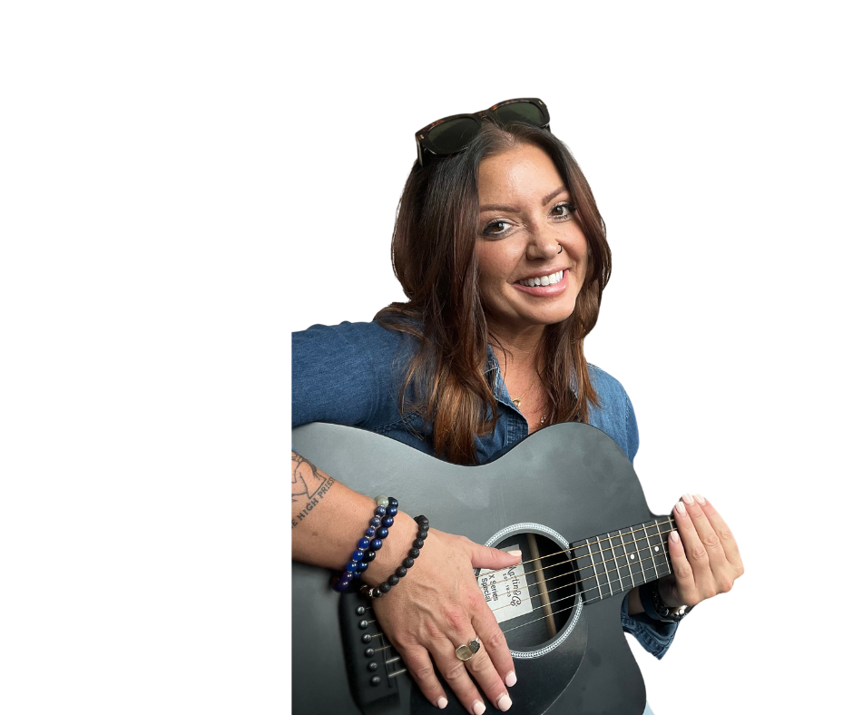 Woman with sunglasses on head smiling while playing a black guitar.