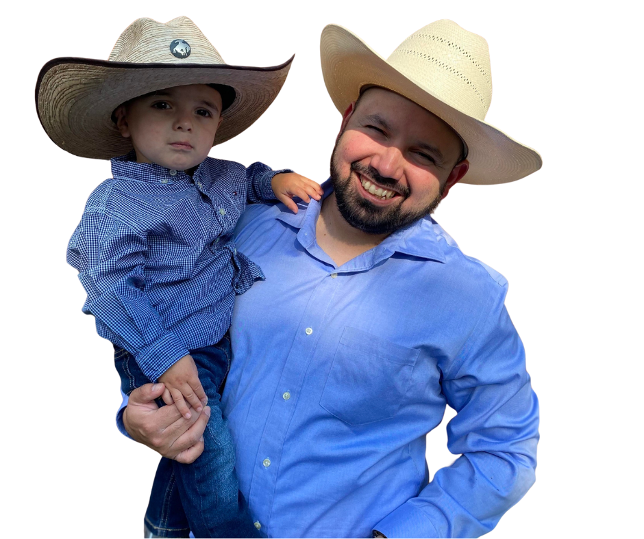 Man holding a child, both wearing cowboy hats and blue shirts, smiling in an outdoor setting.