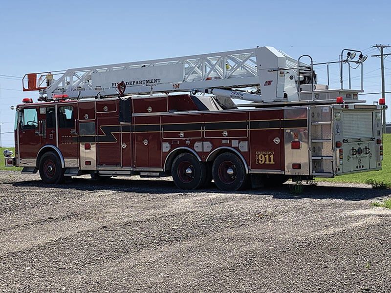 Red and silver fire truck with extended ladder, parked on gravel, sunny day.