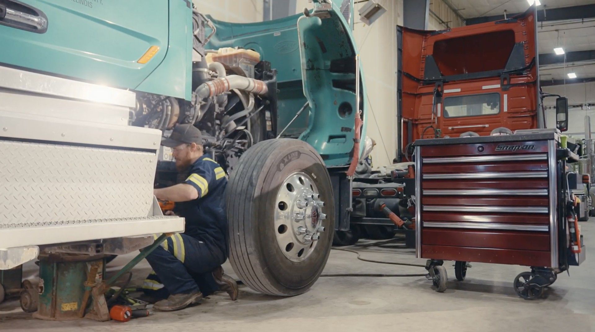 Truck on a lift inside a repair shop. White cab visible, surrounded by blue machinery.