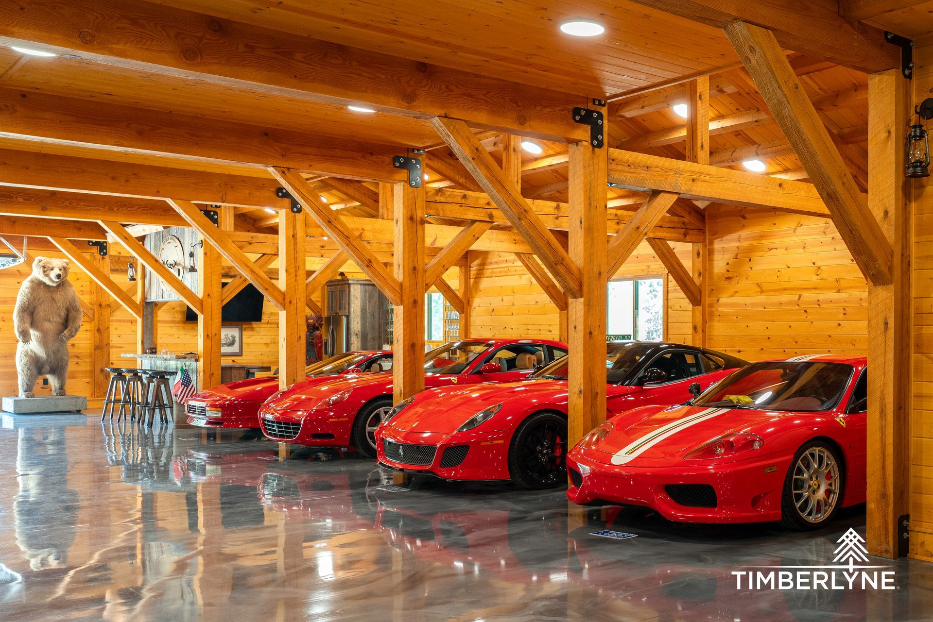 A row of red sports cars parked in a rustic timber-frame garage with a wooden interior and polished concrete floor.