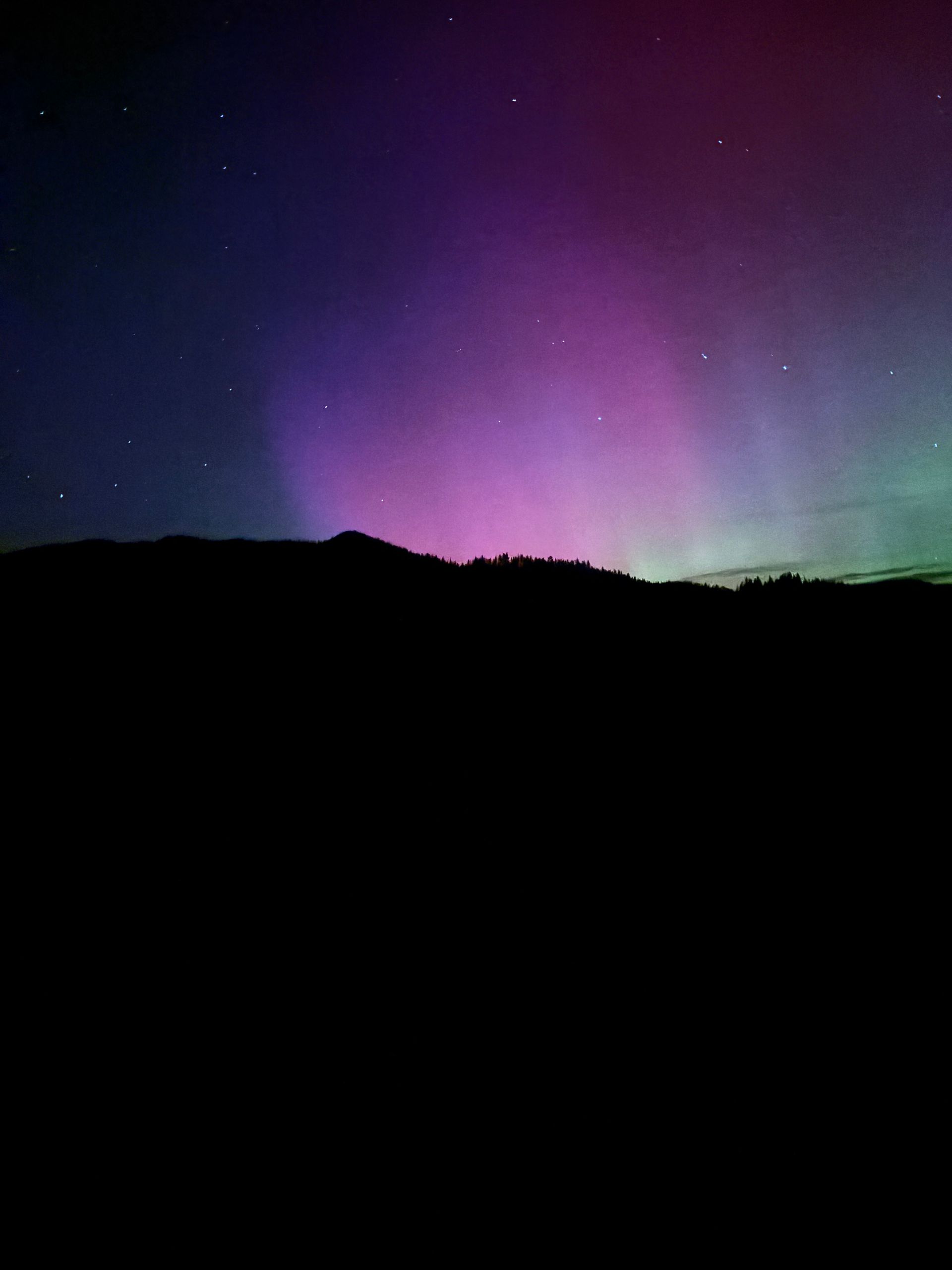 Aurora glowing purple and green above a dark mountain silhouette at night