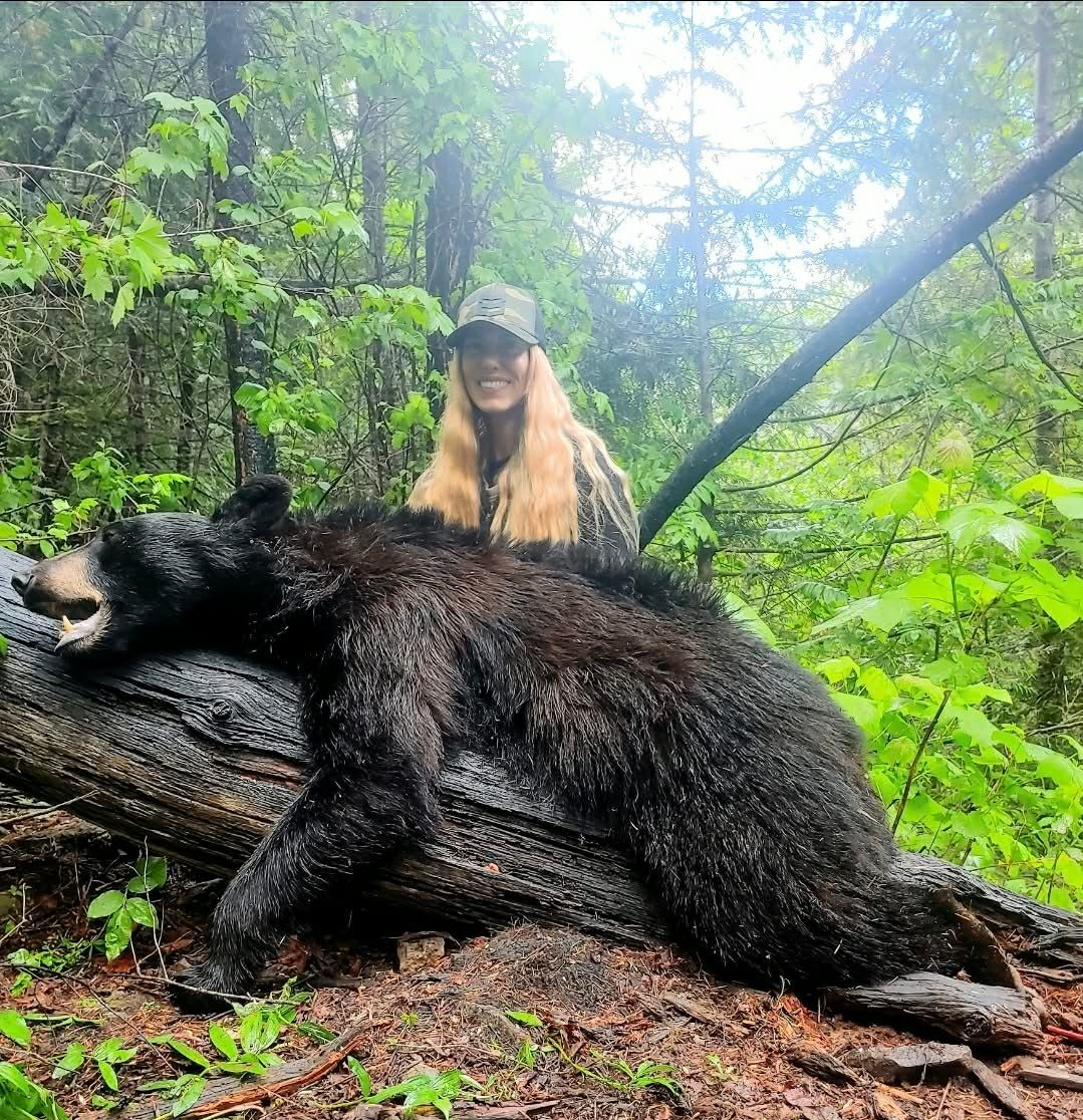 Woman posing beside a large wild boar in a wooded, rainy forest.