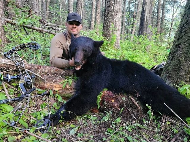 Hunter kneeling beside a large black bear in a forest clearing