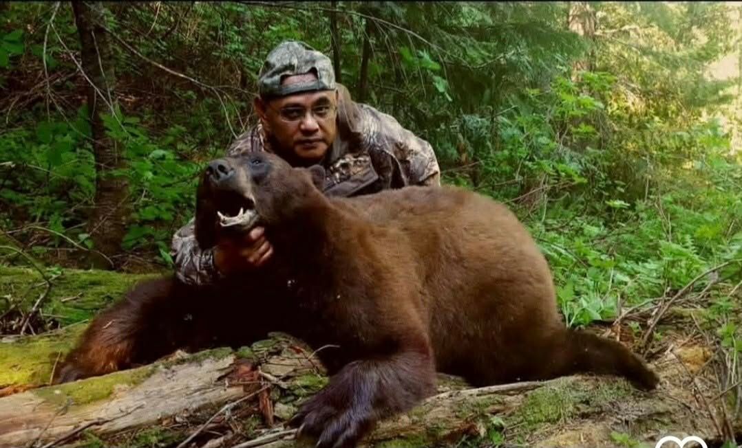 Hunter crouches behind a large bear in a forest, with the bear snarling in the foreground.