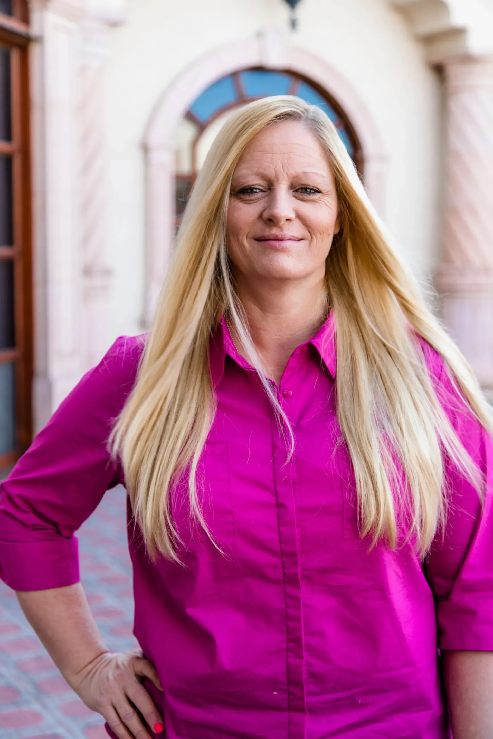 A woman in a pink shirt is standing with her hands on her hips.