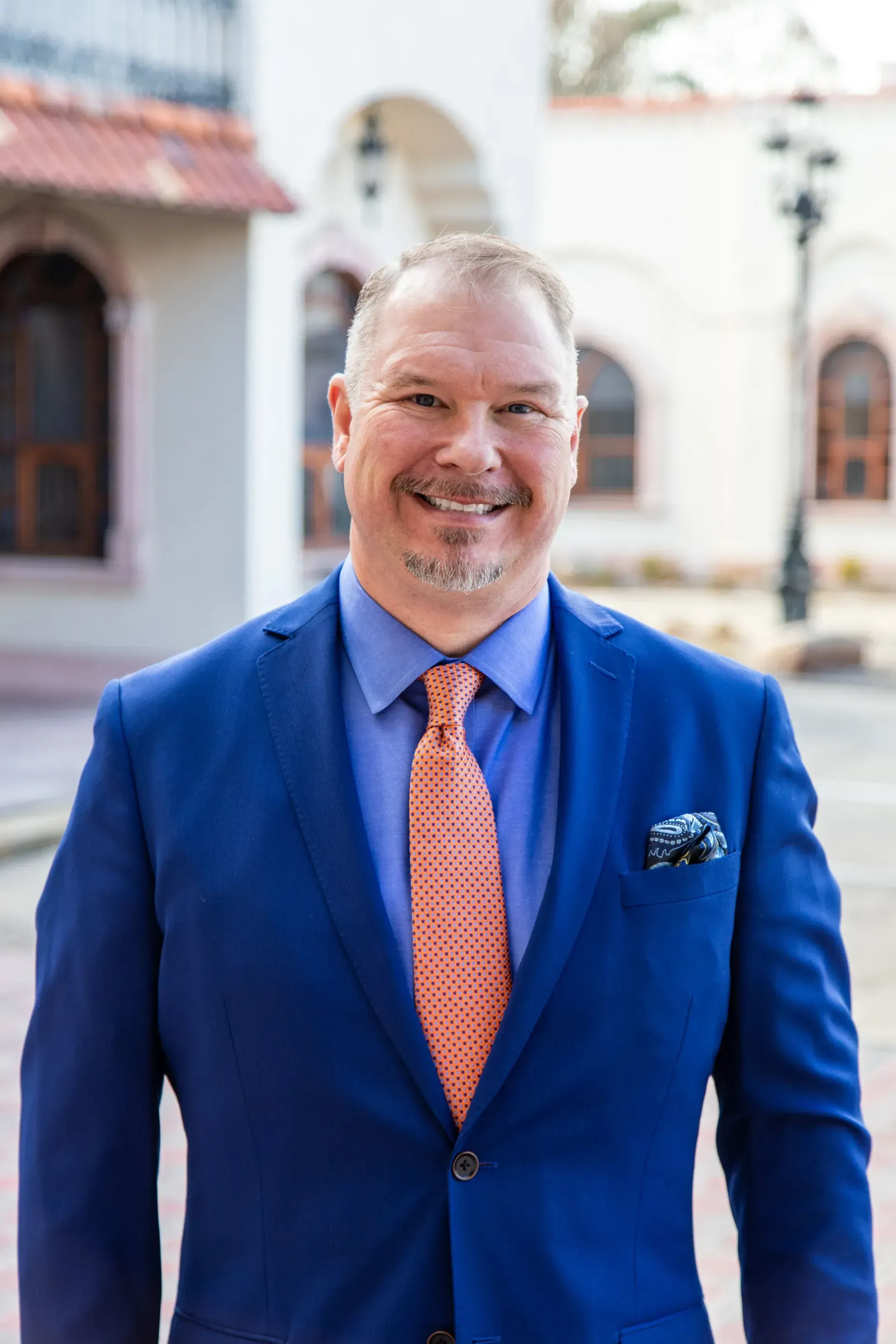 A man in a blue suit and orange tie is smiling for the camera.
