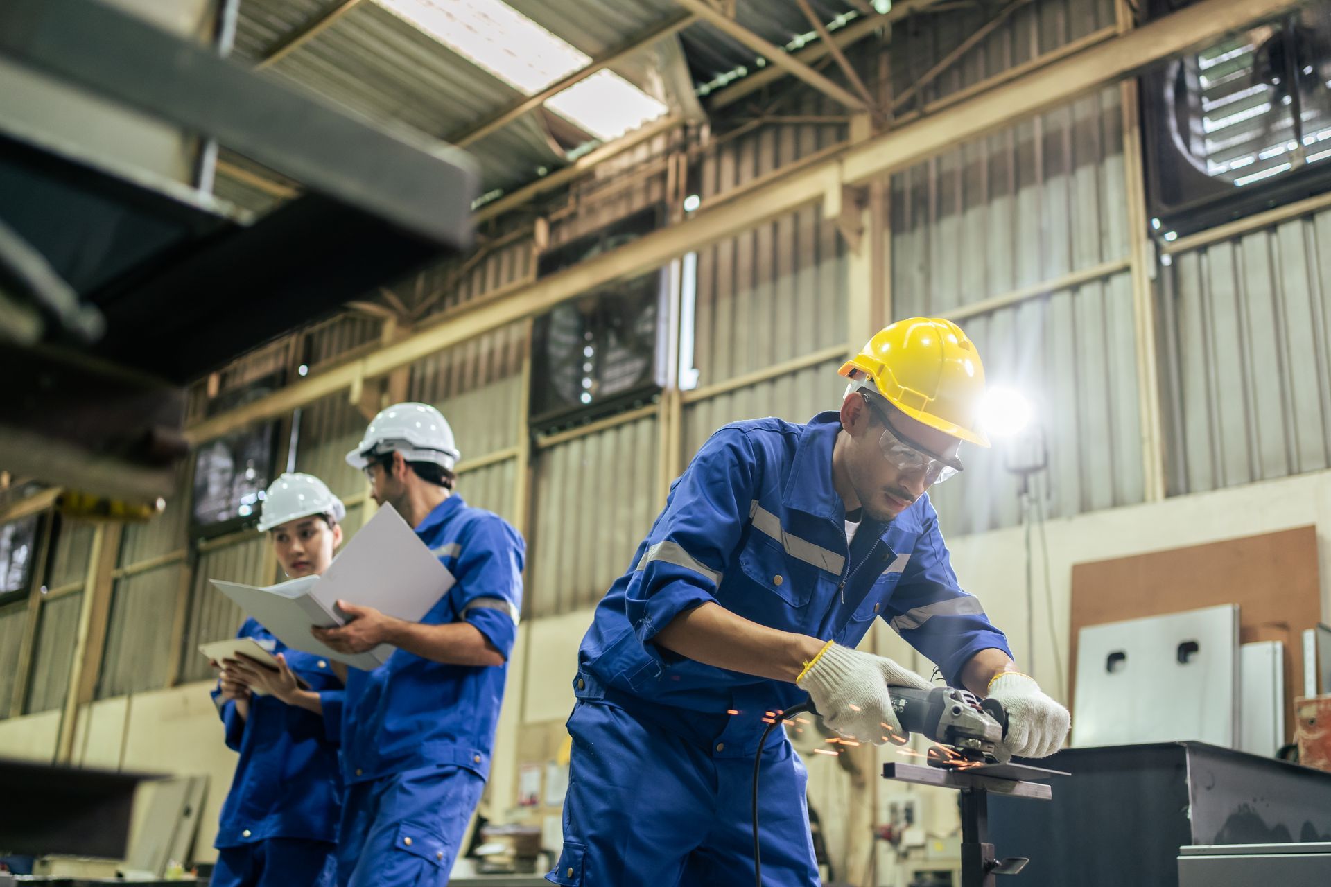 Workers in blue coveralls and hard hats assembling equipment in an industrial workshop