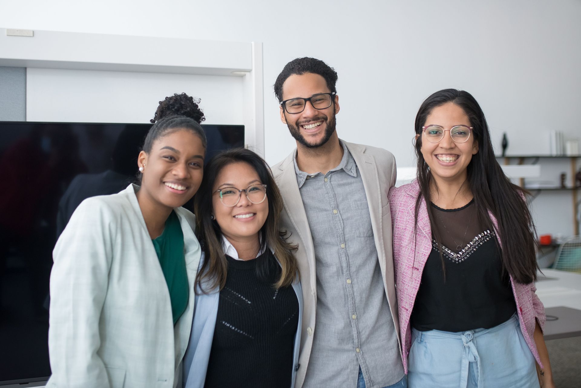 Four smiling colleagues posing together in a modern office lounge.
