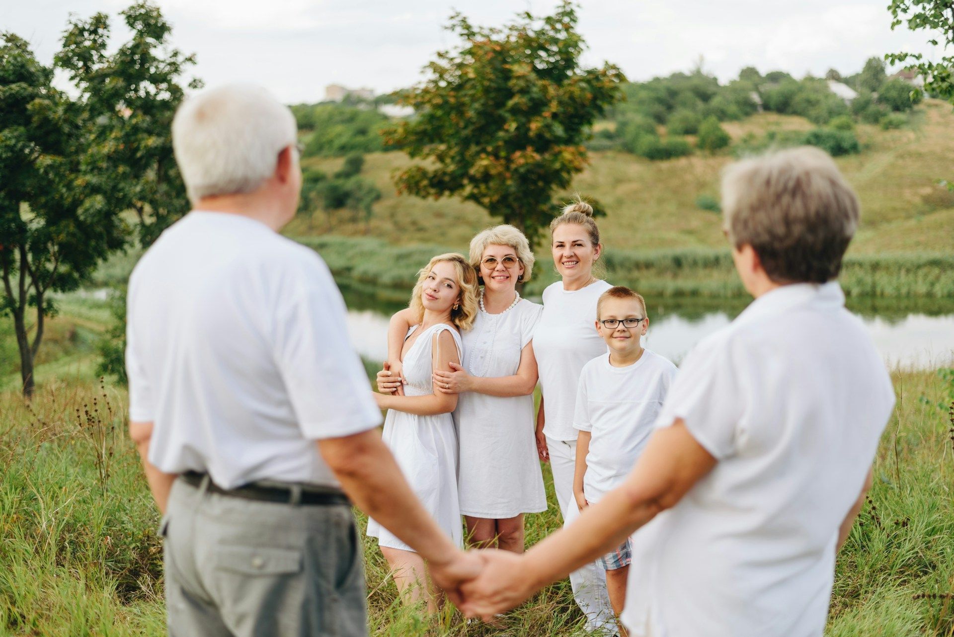 Group holding hands in a grassy field, smiling at each other outdoors.