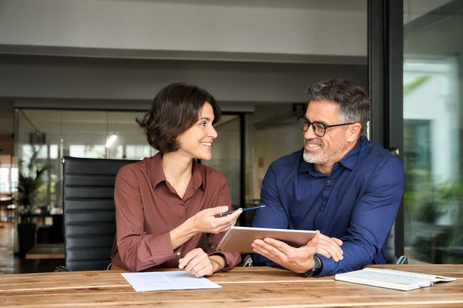 Two colleagues smiling and reviewing documents at a conference table in an office