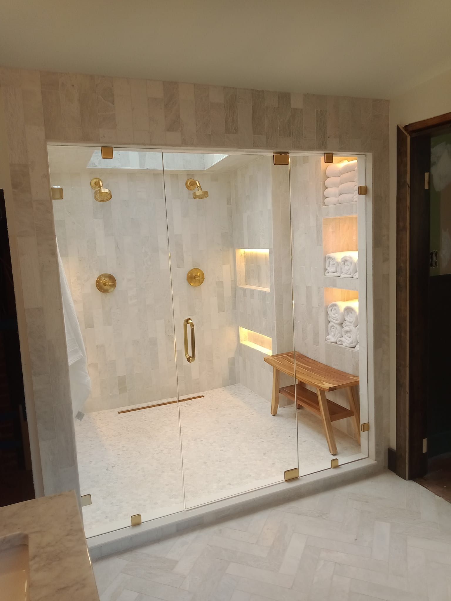 A bathroom with a glass shower door and a wooden bench
