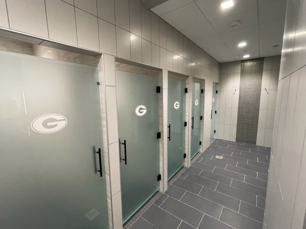 A hallway with a row of shower stalls with frosted glass doors.