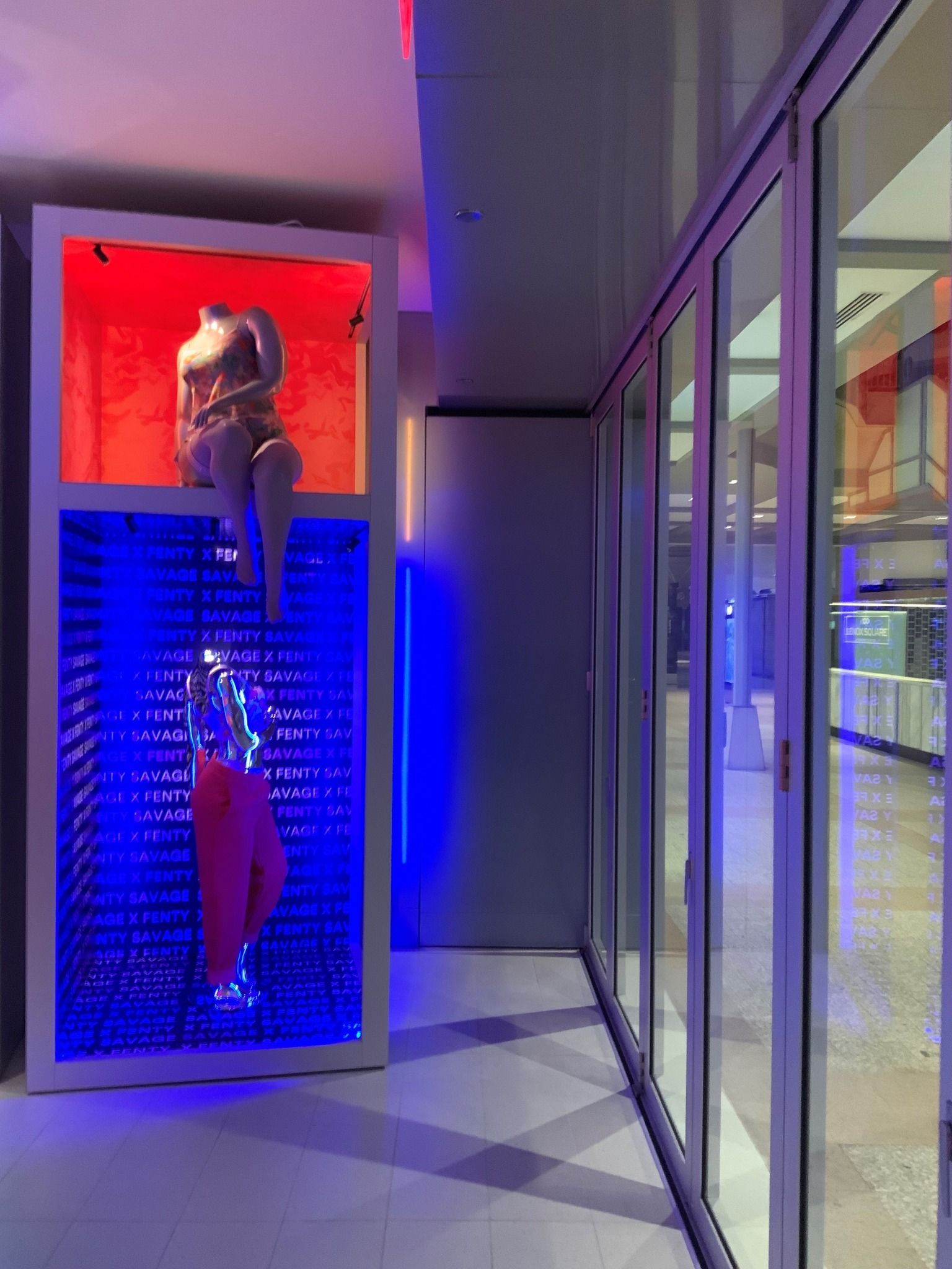 A mannequin is standing in a glass box in a hallway.