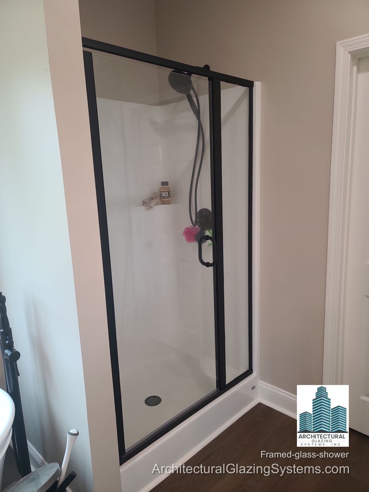 Black-framed glass shower enclosure with a black door handle and light-colored shower walls in a Lamar County home.